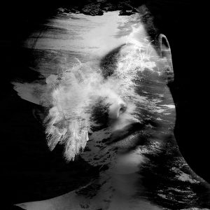 Submerged in the Waves is a black and white portrait of a woman blended with waves crashing onto a reef, from a different angle, her face obscured by the foam